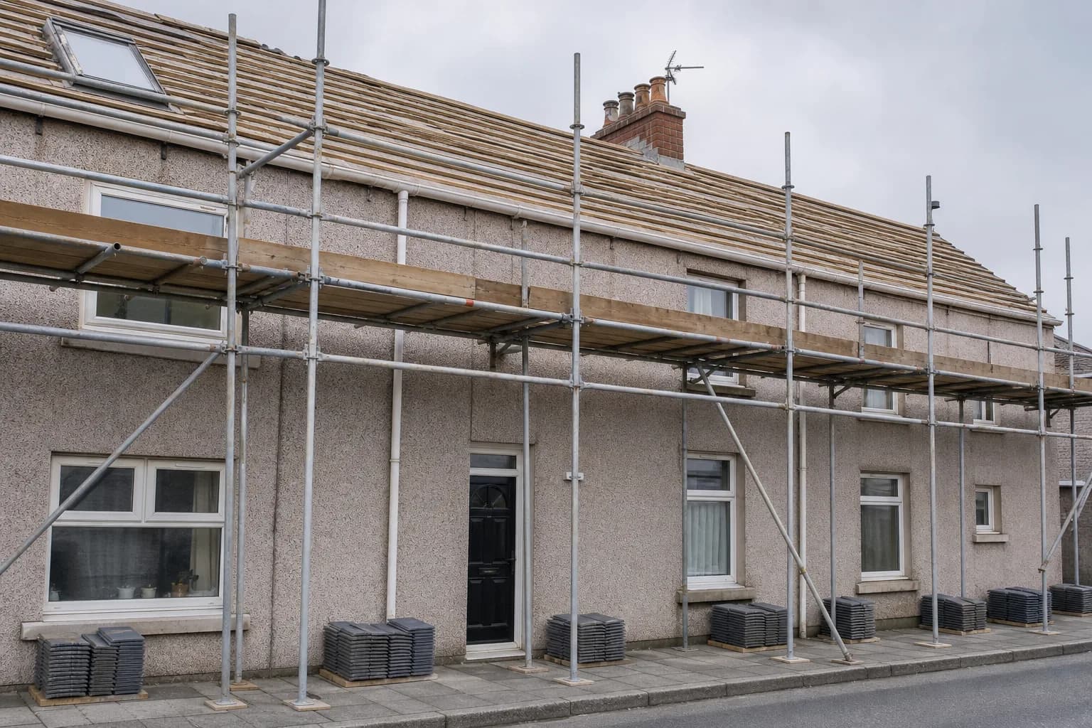 Roofing scaffolding, stacked slate tiles and a work van on a residential street